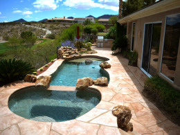 Image of wide-cut flagstone overlay concrete pool deck with natural rock features.